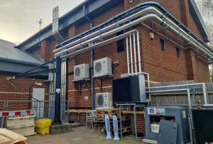 A picture of the outside of a sports centre with air source heat pumps and other appliances on the wall