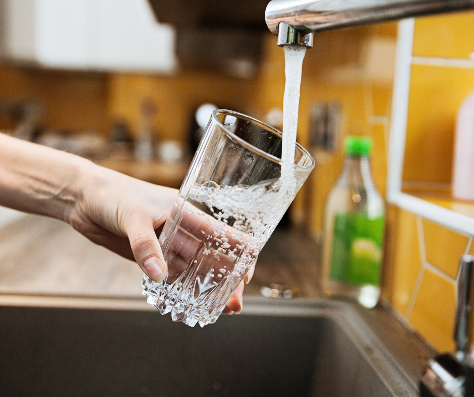 Hand holding a glass under a running kitchen tap as water fills the glass.
